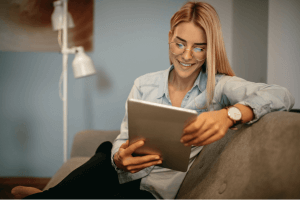 Woman Wearing Glasses On Couch Smiling At Ipad