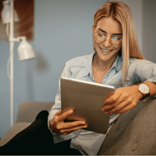 Woman Wearing Glasses On Couch Smiling At Ipad