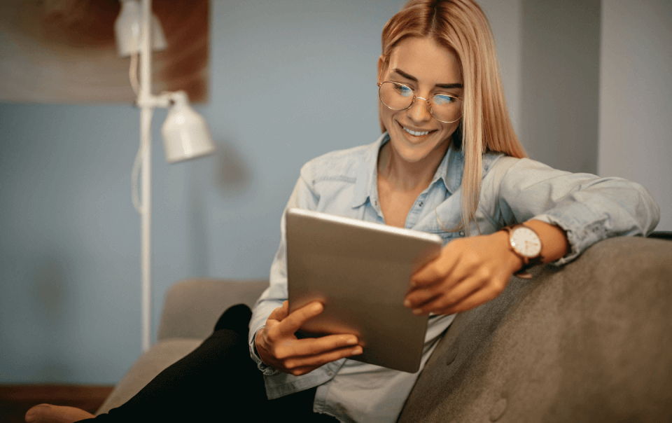 Woman Wearing Glasses On Couch Smiling At Ipad