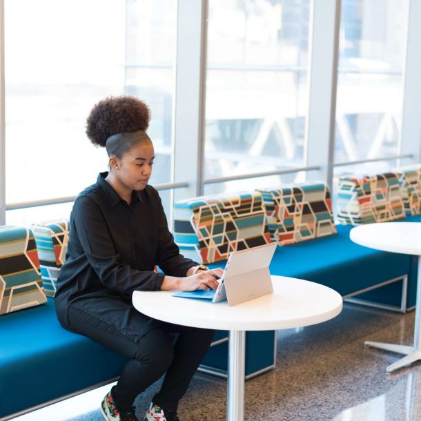 Young Woman Sitting on Blue Chair Working on a Laptop in Office Building for Building Better Agents